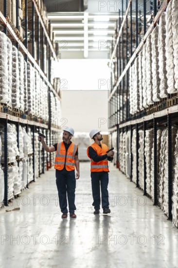 Warehouse workers in high visibility vests and hard hats checking inventory and managing logistics operations using barcode scanners in a modern distribution center
