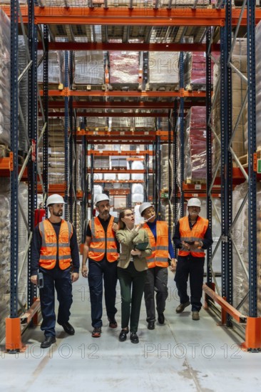 Female warehouse manager and diverse team of logistics workers are collaborating and inspecting stock inventory while walking through a large industrial storage facility