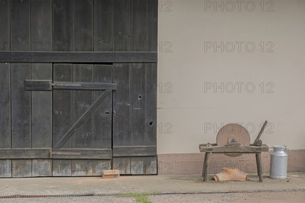 A whetstone and a bucket in front of an old rustic barn door, Hohwiller, Alsace, France