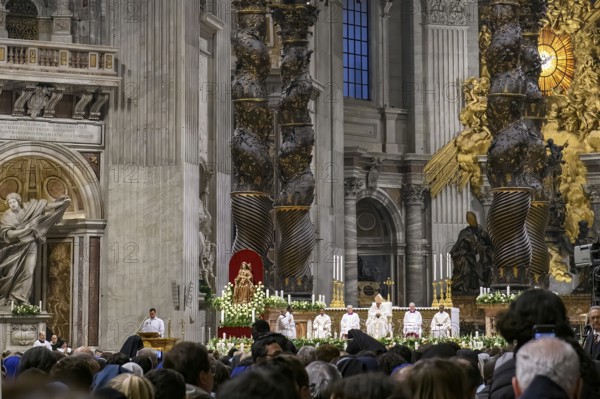 View of heads of faithful in the foreground at the bottom of the picture Pope Saint Father with white robe and mitre on head between columns of canopy by Bernini over the tomb of Peter celebrates Saint Mass in St. Peter's Basilica, Basilica of St. Peter, Vatican, Rome, Lazio, Italy