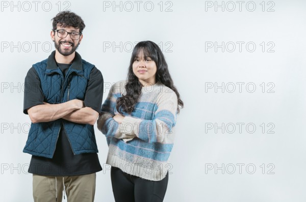 Smiling young couple with crossed arms looking at camera, isolated. Cheerful young multiethnic couple with arms crossed, isolated
