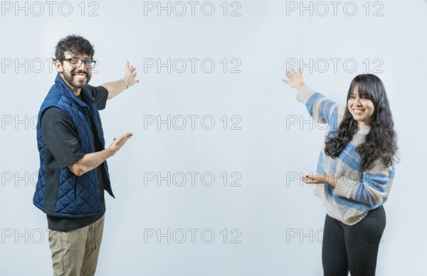 Happy couple showing something and smiling at the camera, isolated. Young couple presenting something smiling at camera