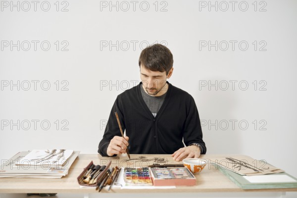 An artist is focused on creating artwork at a neatly organized table
