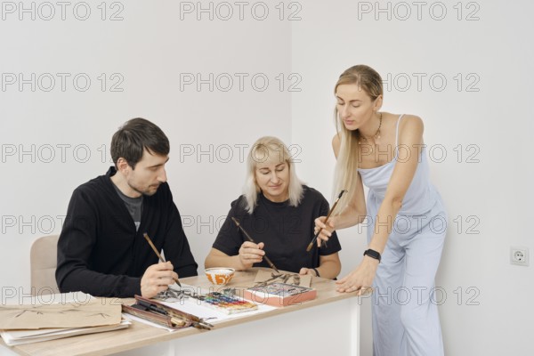 Three artists are engaged in a creative painting workshop. They share techniques and ideas while working on their projects at a bright, minimalist studio space during a sunny afternoon