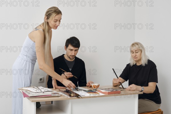 Three artists focus intently on their painting project in a well-lit studio