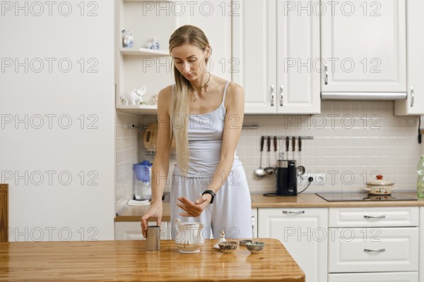 A woman pours tea leaves into a teapot, preparing to prepare aromatic tea in the kitchen