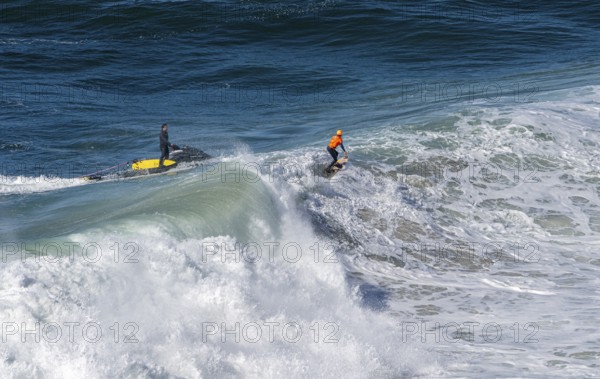 Surfers with their jet ski pilots in the Atlantic waves below Farol de Nazaré, Forte São Miguel, known as a surfer hot spot with monster waves between November and February of each year, Nazaré, Portugal
