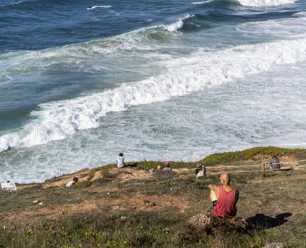 Tourists watch the waves of the Atlantic on the rocky plateau of Sito, also known as Forte São Miguel, a surfing paradise with monster waves in the months of November to February, Nazaré, Portugal