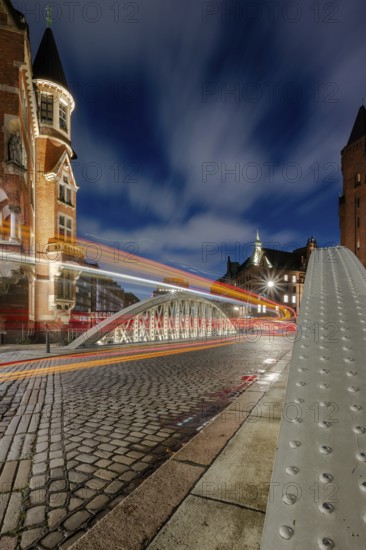 Blue hour and traces of light in the Speicherstadt Hamburg on the Neuerwegsbrücke with cobblestones in the foreground and moving clouds in the background, Hamburg, Germany