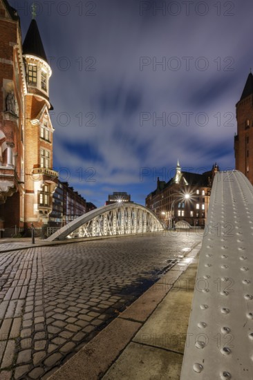 Blue hour in the Speicherstadt Hamburg on the Neuerwegsbrücke with cobblestones in the foreground and moving clouds in the background, Hamburg, Germany