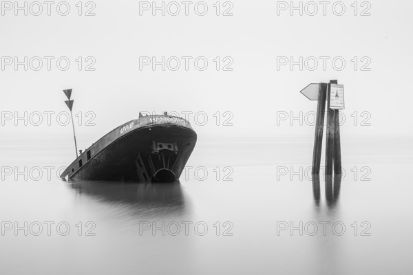 Long exposure of the partially sunken MS Uwe shipwreck in the Elbe on Falkensteiner Ufer in fog and calm water in black and white, Blankenese, Hamburg, Germany