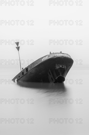 Long exposure of the partially sunken MS Uwe shipwreck in the Elbe on Falkensteiner Ufer in fog and calm water in black and white, Blankenese, Hamburg, Germany