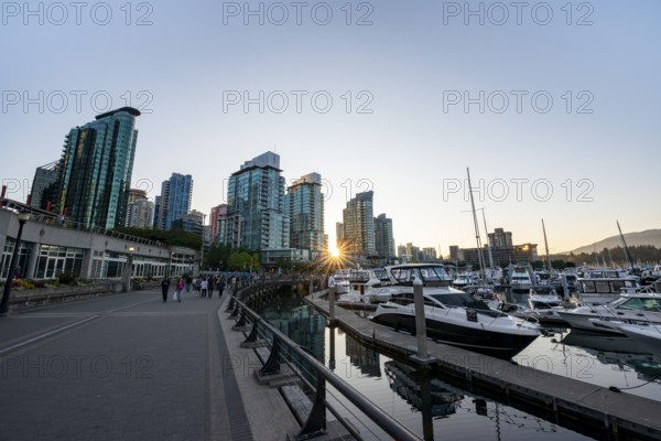 Boats in marina at sunset, skyscrapers on promenade with sun star, Coal Harbour, Vancouver, British Columbia, Canada