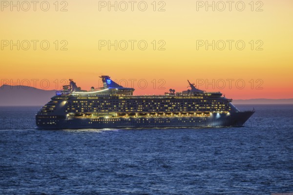 Mykonos, Cyclades, Greece - Voyager of the Seas cruise ship sails from Mykonos harbour bay towards the evening sun at dusk