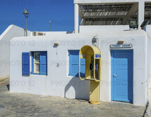 Mykonos, Cyclades, Greece - Old yellow telephone box in front of white house with blue shutters in the old town alleys of Mykonos Town. Mykonos is part of the Cyclades archipelago in the Aegean Sea