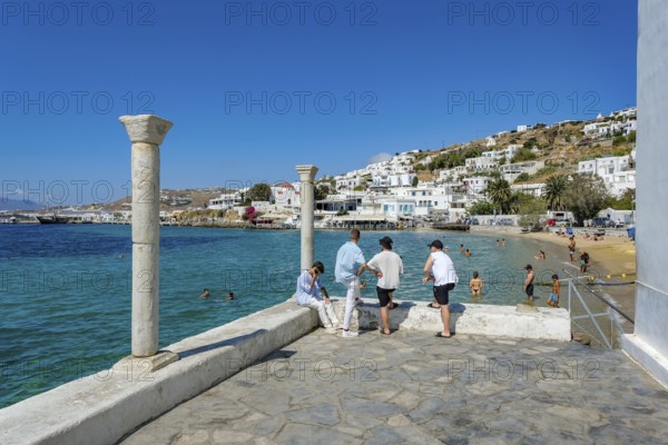 Mykonos, Cyclades, Greece - Young people on the small town beach Paralia Cheras Mikonou right at the old port in the old town of Mykonos Town, Mykonos Chora. Mykonos is part of the Cyclades archipelago