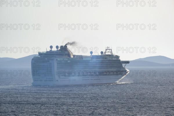 Mykonos, Cyclades, Greece - Cruise ship AZURA from the shipping company P&O Cruises sails out of Mykonos harbour bay and leaves behind a dark cloud of exhaust gas. The M/S Azura can accommodate up to 3100 passengers. The 290 m long ship was last modernized in 2018, following its maiden voyage in 2010