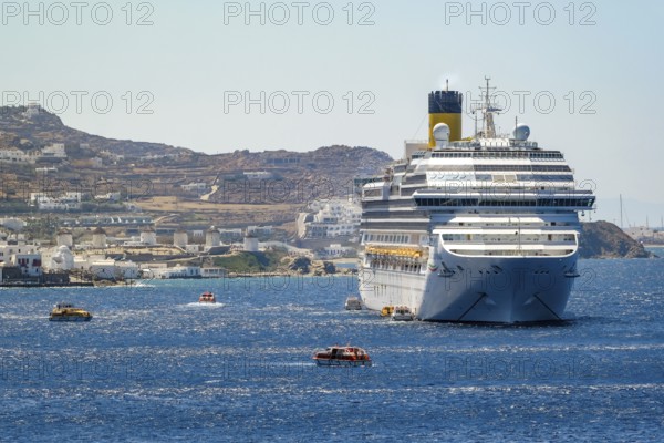 Mykonos, Cyclades, Greece - Cruise ship COSTA FORTUNA is located in the bay against the backdrop of the old town with the landmark of the six windmills, Mykonos Town. Cruise ships bring tourists to shore
