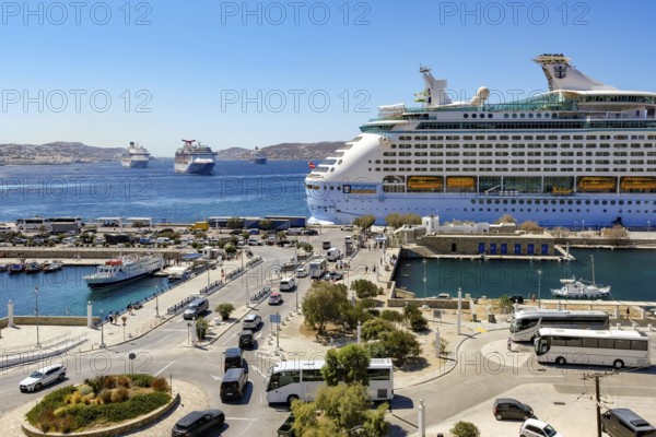 Mykonos, Cyclades, Greece - Mykonos New Port, cruise ship is moored on the quay in the new port in front of the skyline of Mykonos Town. At the back, there are more cruise ships in the bay off Mykonos City with a view of the old town with the windmills. Cruise ships bring tourists to the old town