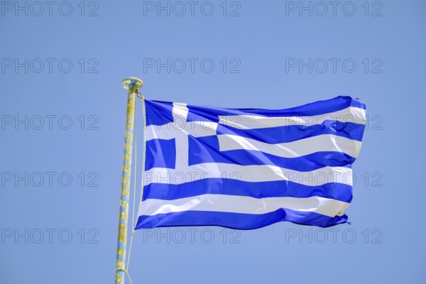 Ano Mera, Mykonos, Cyclades, Greece - Greek national flag fluttering on the flag pole on the roof of Panagia Tourliana monastery forms the center of Ano Mera. The men's convent from the 16th century on the village square in the interior of the island is now a tourist attraction much visited by tourists