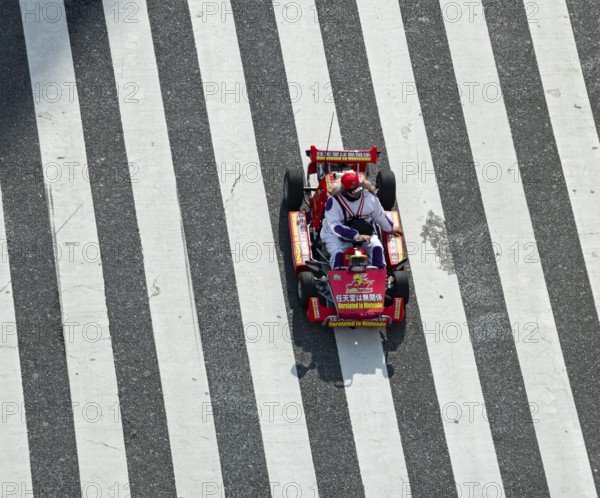 People in costumes drive small go-kart racing cars across zebra crossings, Shibuya Crossing, Shibuya, Tokyo