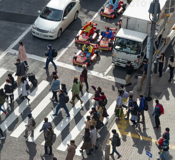 People cross zebra crossings, people in costumes ride small go-kart racing cars, Shibuya Crossing, Shibuya, Tokyo
