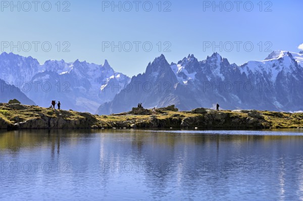 A group of hikers at Lac de Chésserys, behind the snow-covered Mont Blanc massif, Chamonix-Mont-Blanc, Haute-Savoie, France