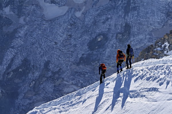 Three ascended mountaineers run across a snow-covered mountain ridge, Aiguille du Midi, Chamonix-Mont-Blanc, Haute-Savoie, France