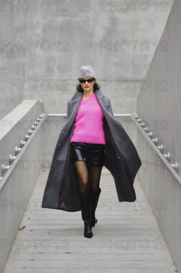 Model walks confidently in urban fashion featuring bright pink sweater and stylish coat