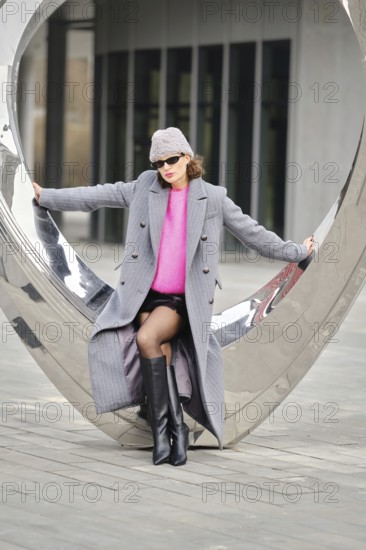 A woman poses confidently in an urban environment, showcasing vibrant clothing against contemporary architecture