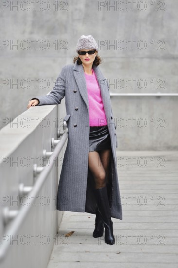 A stylish model poses confidently in an urban setting, wearing a vibrant pink sweater under a gray coat
