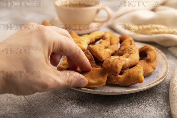 Crunchy biscuit Brushwood cookies with hand sprinkled with powdered sugar on brown concrete background and linen textile, cup of coffee, side view, selective focus