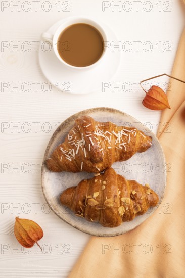 Croissant on blue plate on white wooden background and orange linen textile, cup of coffee, top view, flat lay, close up