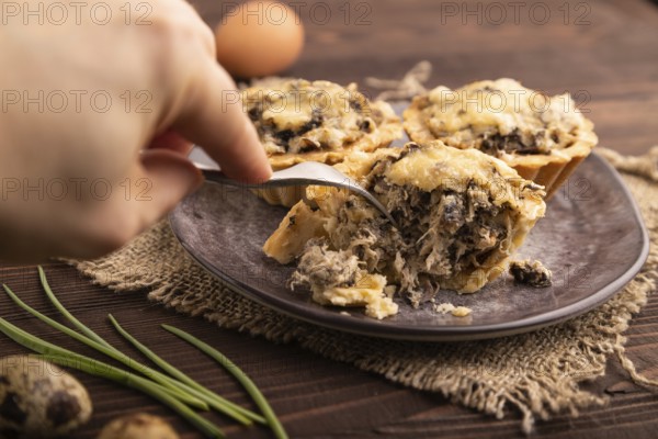 Tartlets with meat and cheese with hand on brown wooden background and linen textile. side view, close up, selective focus