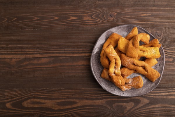 Crunchy biscuit Brushwood cookies sprinkled with powdered sugar on brown wooden background, top view, flat lay, copy space