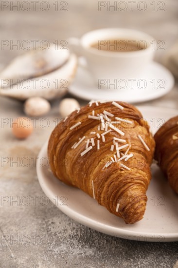 Croissant on white plate on brown concrete background and linen textile, cup of coffee, side view, close up, selective focus