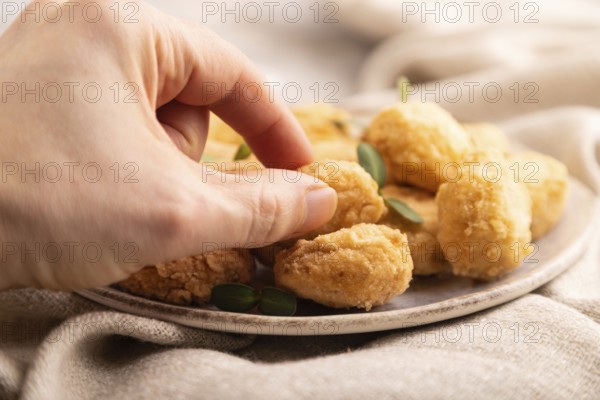 Fried crispy Chicken Nuggets with ketchup, microgreen on brown concrete background and linen textile with hand. side view, close up, selective focus