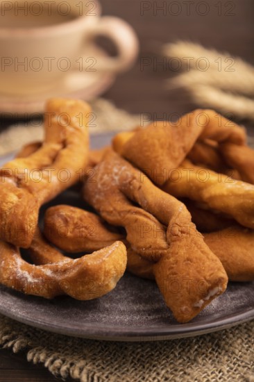 Crunchy biscuit Brushwood cookies sprinkled with powdered sugar on brown wooden background and linen textile, cup of coffee, side view, close up, selective focus