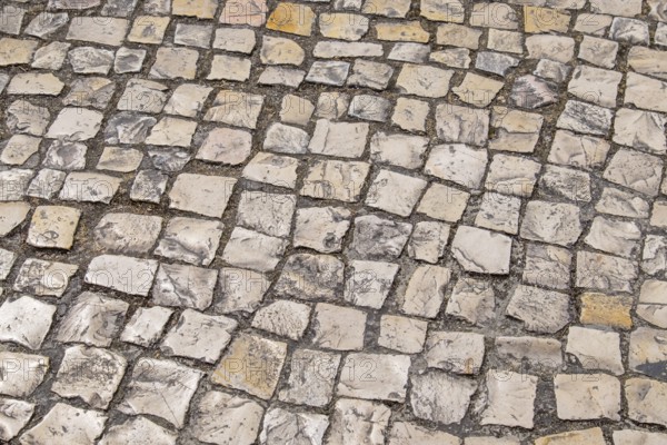 Irregular paving stones in shades of beige and gray create an antique street texture, Portugal