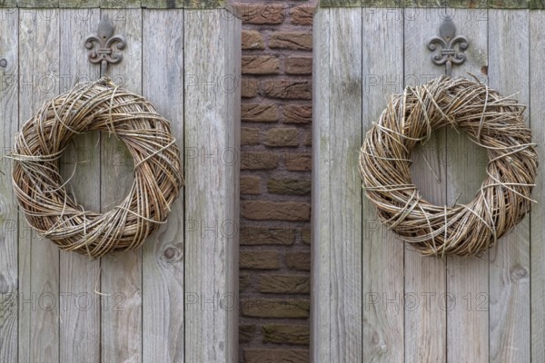 Two decorative wreaths made of branches hang symmetrically on a rustic wooden board in front of a brick wall, Münsterland, North Rhine-Westphalia, Germany