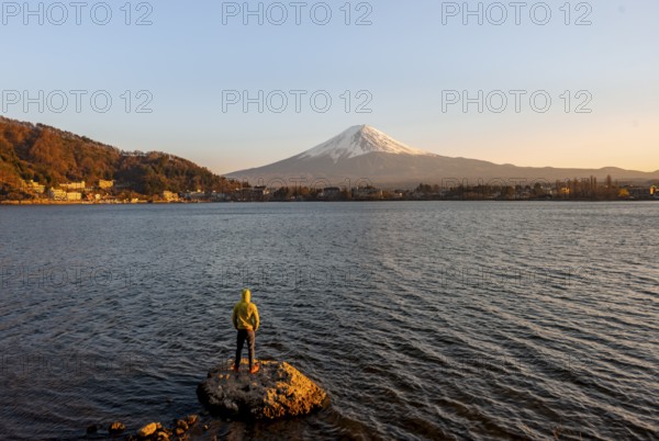 Young man standing on rocks in Lake Kawaguchi, view of Mount Fuji volcano at sunset, Yamanashi Prefecture, Japan