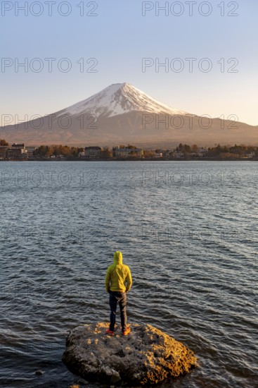 Young man standing on rocks in Lake Kawaguchi, view of Mount Fuji volcano at sunset, Yamanashi Prefecture, Japan