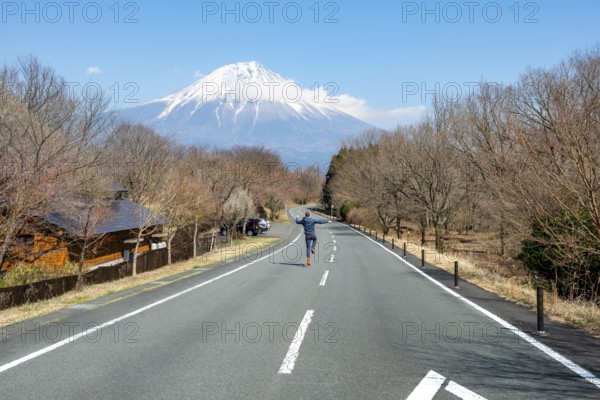 Young man jumping on road, road leading to Mount Fuji volcano, wanderlust, Yamanashi Prefecture, Japan