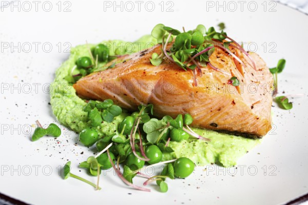 Delicious grilled salmon is placed elegantly on creamy green pea puree. Fresh microgreens and peas add a bright touch, creating an appetizing dish perfect for any meal
