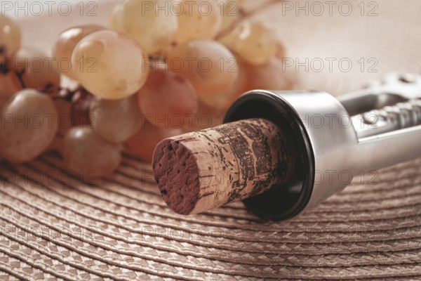 A corkscrew with a wine bottle stopper, lying on a woven napkin, with green grapes