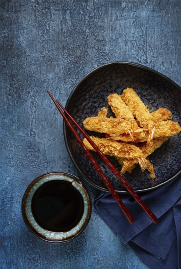 Shrimp in tempura, deep fried, on a black plate, with soy sauce, close-up, top view, no people