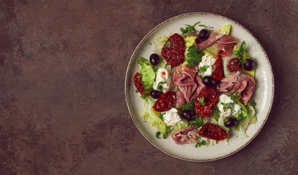Salad with dried tomatoes, prosciutto, soft cheese, olives, homemade, top view