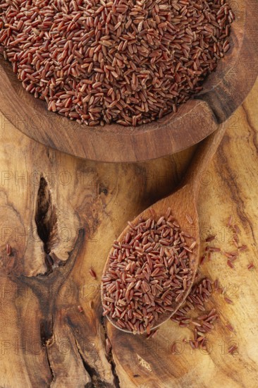 Natural, red rice, in a wooden bowl and spoon on a wooden surface in rustic style, top view