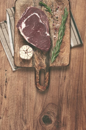 Raw steak, beef steak, rib eye steak, on a cutting board, freshly frozen, with spices and herbs, on the table, top view