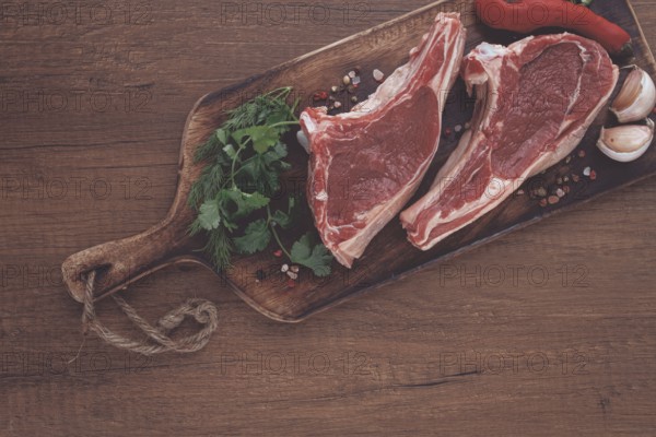 Freshly sliced lamb chops, with herbs and vegetables, on a wooden board, ready to cook, on a wooden table